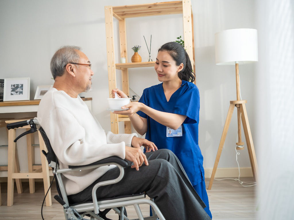 Caregiver assisting elderly woman on sofa in cozy living room, symbolizing the compassionate and personalized approach in Home Care Services.