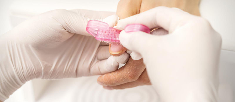 A manicurist using a brush to remove dust from a woman's nails.