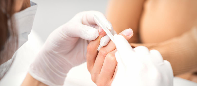 A manicurist filing a woman's nails with a nail file.