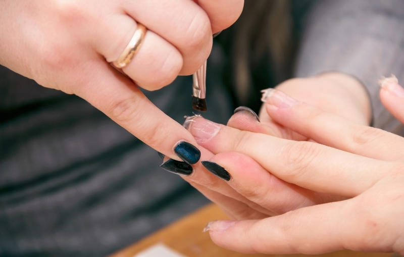 A beautician applying artificial nails to a client's hand in a salon