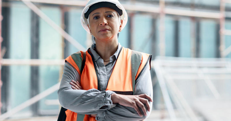 A construction work. A mature engineer stands with arms crossed and observes the progress of the project.