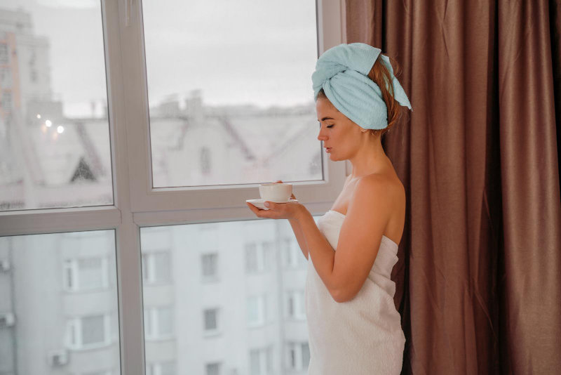 A young woman in a spa bathrobe drinking a hot beverage.