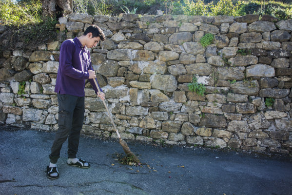 Young man outdoors sweeping foliage with broom