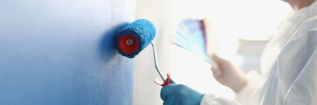 Person painting a white wall using a blue roller