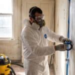 Renovator in a respirator and coverall setting plastic containment for lead-safe paint work in an older home
