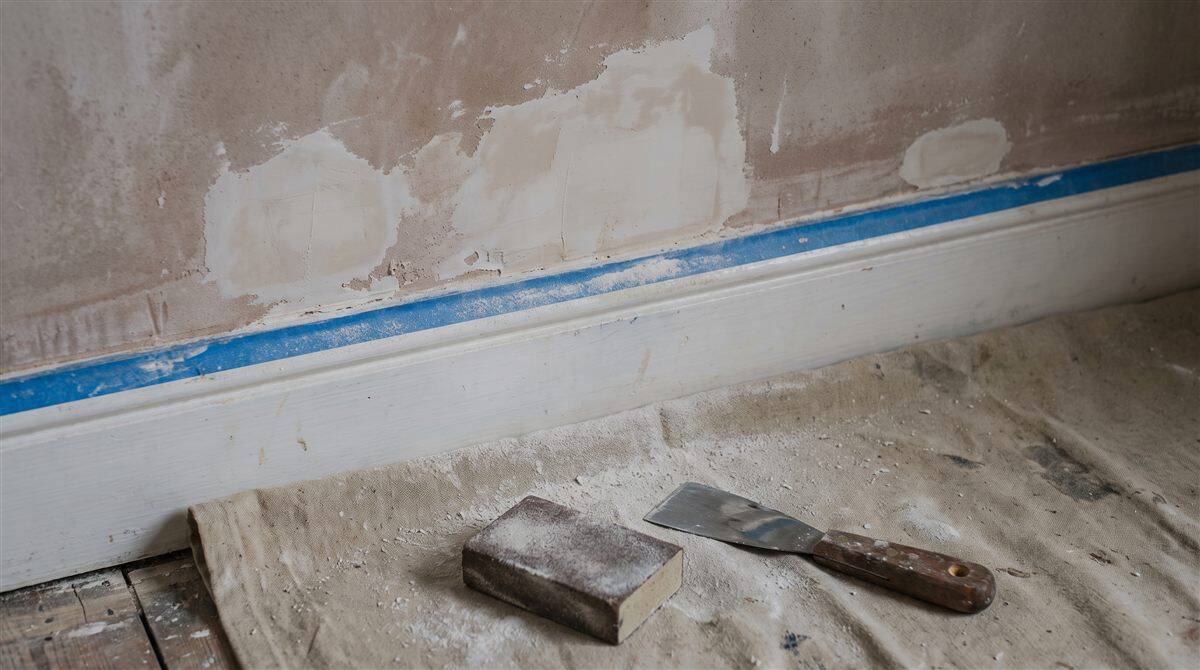 Filled and sanded wall patches with masking tape along a skirting board in a UK interior