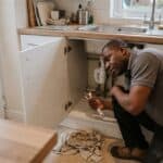 Plumber working on waste pipework under a kitchen sink in a UK home