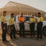 Plumbing business owner hands out letters to his crew beside a ute on a Brisbane building site