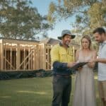Builder in a hi-vis shirt reviews a contract with a couple outside their home extension