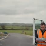 Subcontractor in hi-vis reads paperwork at the open door of a van on a new-build estate