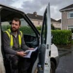 Electrician sitting in the open door of his van outside a Galway house, reading a bank statement