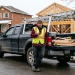 One-man framing contractor checking his phone beside his pickup on a snowy Ontario street, the case where WSIB for contractors is mandatory